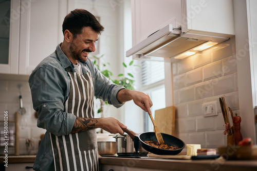 Obraz na plátně Happy man preparing food in frying pan in kitchen.