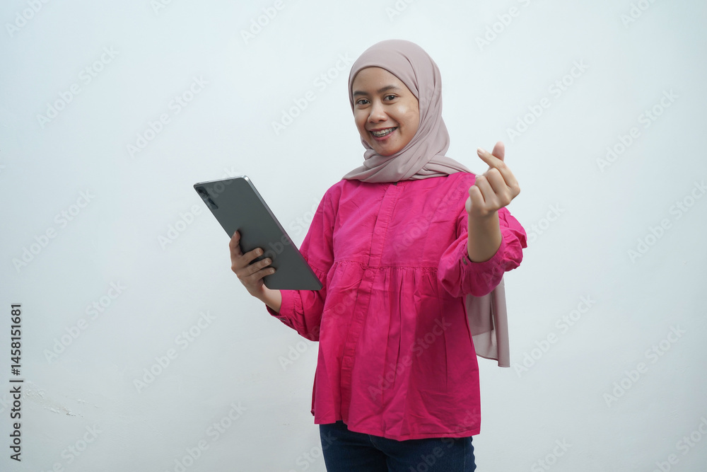 Smiling Asian Muslim Woman Making Finger Heart Gesture While Holding Tablet Against White Background Smiling Asian Muslim Woman Making Finger Heart Gesture While Holding Tablet Against White Background