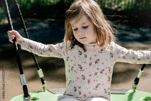 Sad toddler girl on swing, playground. Education, activity outdoor