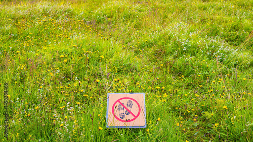 Signpost depicting footsteps crossed with red line in circle. Sign forbids hiking pathway, walking in nature. Nature is protected from entering.