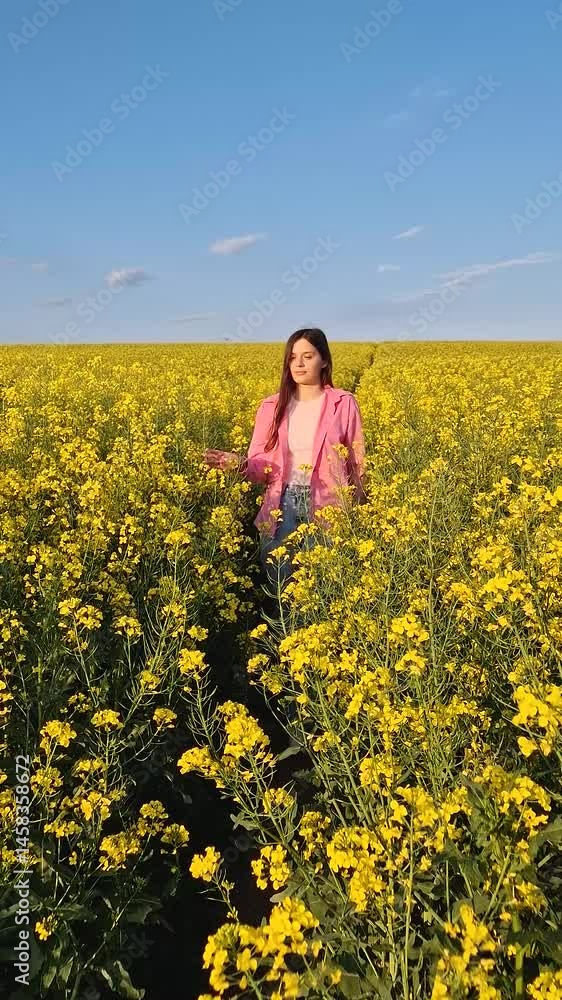 Aesthetic young woman walks a pathway across the rapeseed field, smelling the beautiful yellow flowers. Girl steps elegantly amidst the blooms, adding charm to the picturesque scenery Aesthetic young woman walks a pathway across the rapeseed field, smelling the beautiful yellow flowers. Girl steps elegantly amidst the blooms, adding charm to the picturesque scenery