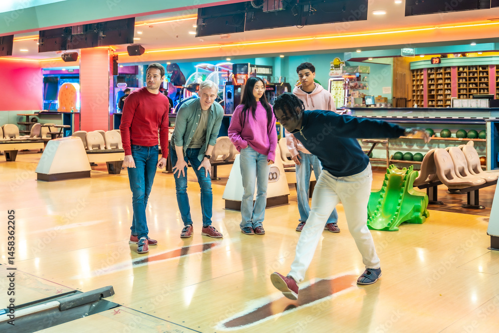 Young man bowling with friends cheering him on
