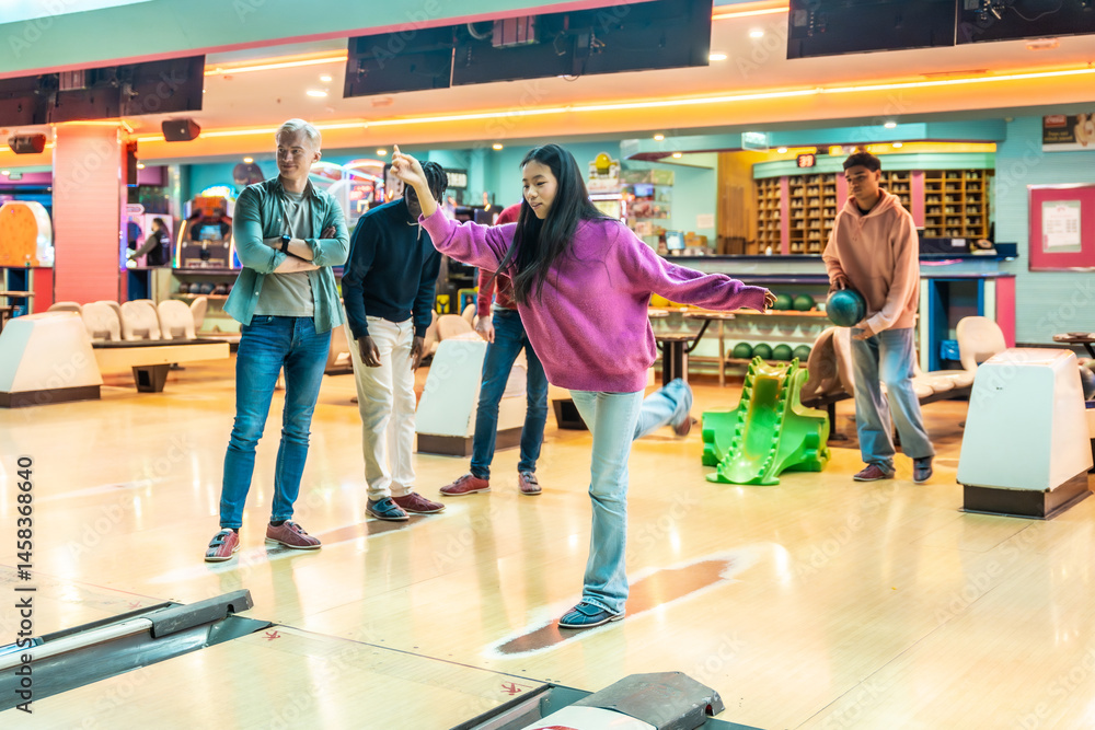Young woman throwing bowling ball with friends watching in bowling alley