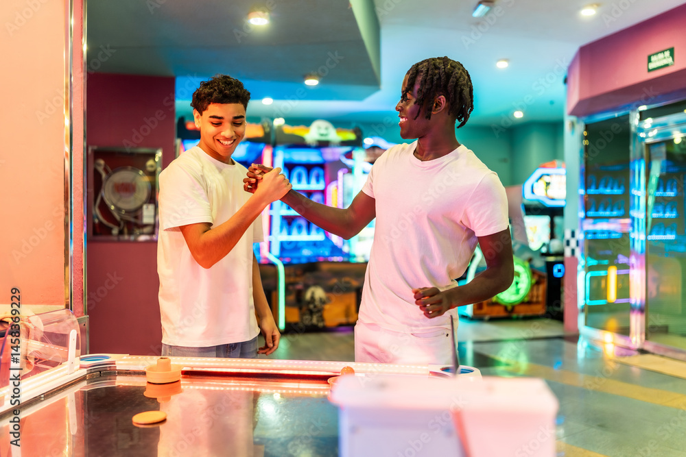 Two young men fist bumping after air hockey game in arcade
