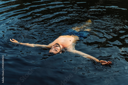Relaxed man floating in natural dark water outdoors