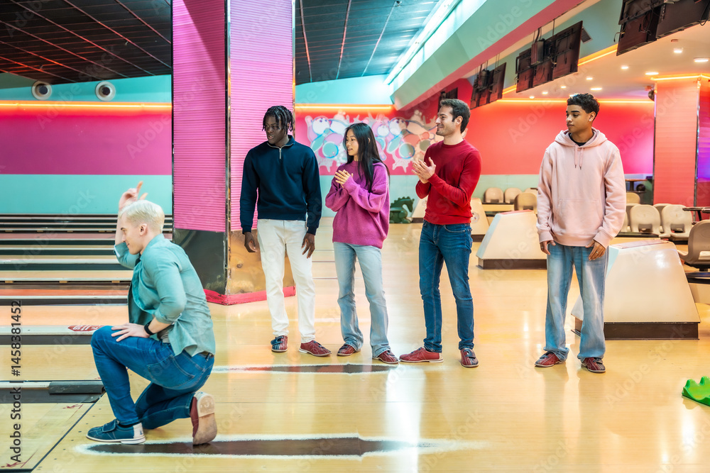 Young man bowling with multiethnic friends cheering and clapping in bowling alley