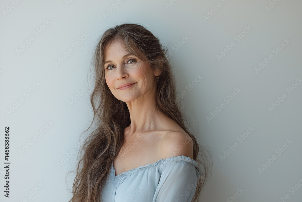 Elegant Mature Woman with Long, Silky Hair in a Soft Blue Dress, Standing Gracefully in Front of a White Wall, Smiling Softly and Gazing Into the Distance. Elegant Mature Woman with Long, Silky Hair in a Soft Blue Dress, Standing Gracefully in Front of a White Wall, Smiling Softly and Gazing Into the Distance.