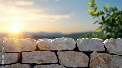 Fototapeta Naklejka Na Ścianę i Meble -  Serene sunset behind a rustic stone wall with soft greenery nearby.