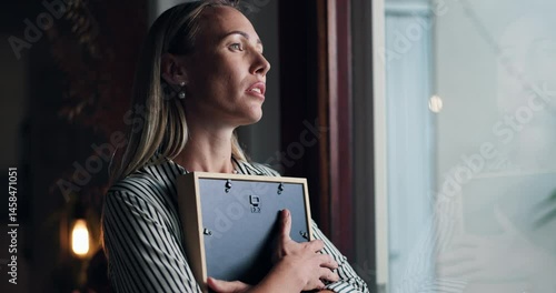 Woman, picture and sad by window at home with memory, mourning and regret or loss of loved one. Female person, widow and hug photo frame with sorrow at house with nostalgia, lonely and reflection