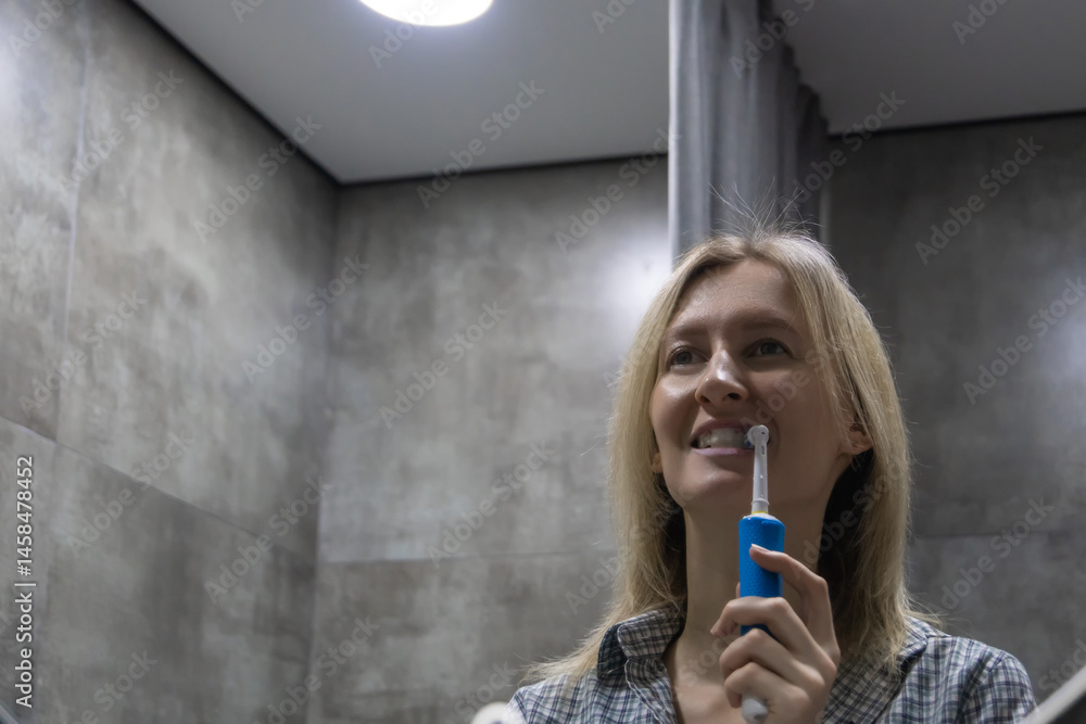 Smiling woman brushing her teeth with an electric toothbrush in a modern bathroom, enjoying her daily oral hygiene routine and promoting dental health