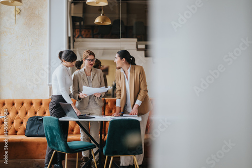 Obraz na płótnie Three women in business attire discussing documents in a stylish and modern office