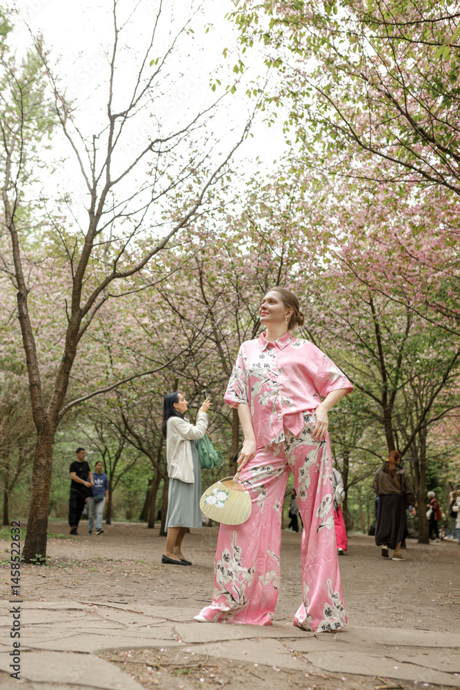 Young woman in pink national costume of Japan, walking in a garden with blooming sakura Young woman in pink national costume of Japan, walking in a garden with blooming sakura