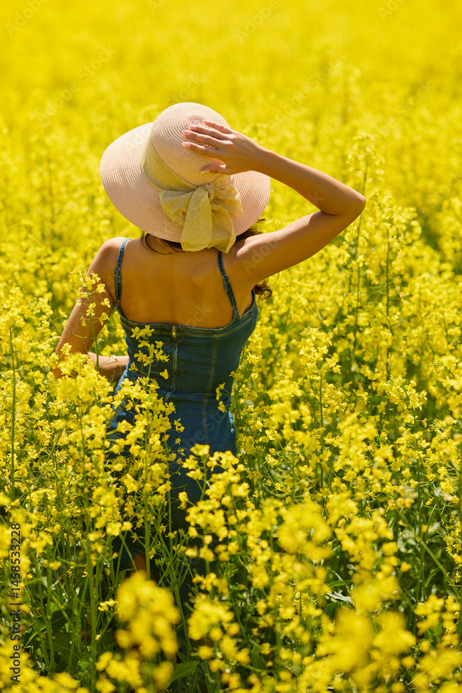 Fototapeta premium beautiful woman with a hat posing in the blooming rapeseed field on a sunny day