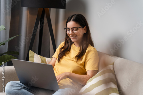 Wellness meets wisdom. Latina Indian woman in her 25s on sofa with laptop, focused on virtual therapy or study session, merging self-care and remote learning in a calm home space