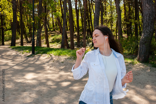 Wallpaper Mural Young caucasian female in white shirt joyfully dancing outdoors with earphones among trees in sunlit park path. Digital nomad lifestyle. Remote work Torontodigital.ca