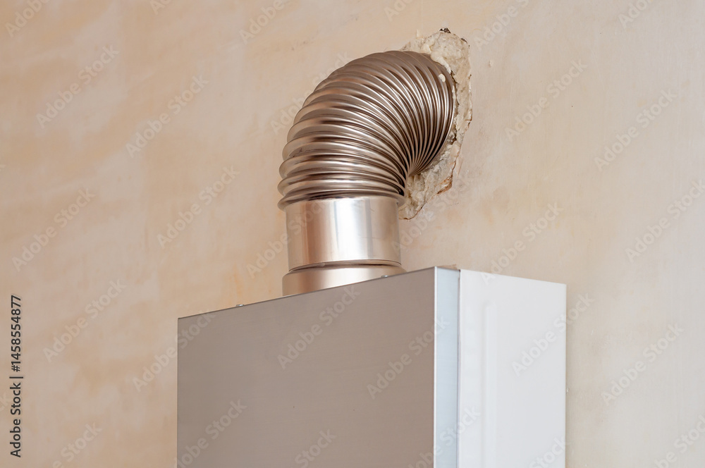 Close-up of a gas boiler showing a corrugated metal flue pipe through a plaster wall opening.