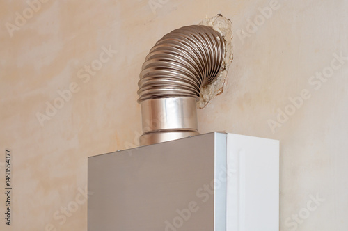 Obraz na płótnie Close-up of a gas boiler showing a corrugated metal flue pipe through a plaster wall opening. w salonie