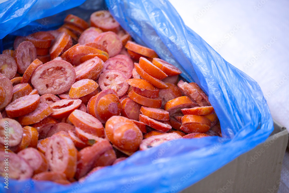 Close-up of shock-frozen sliced red tomatoes with a thin ice coating. Are prepared for retail packaging to ensure extended shelf life in supermarkets and maintain perishable harvest quality.