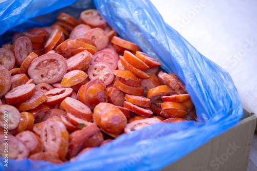 Close-up of shock-frozen sliced red tomatoes with a thin ice coating. Are prepared for retail packaging to ensure extended shelf life in supermarkets and maintain perishable harvest quality.