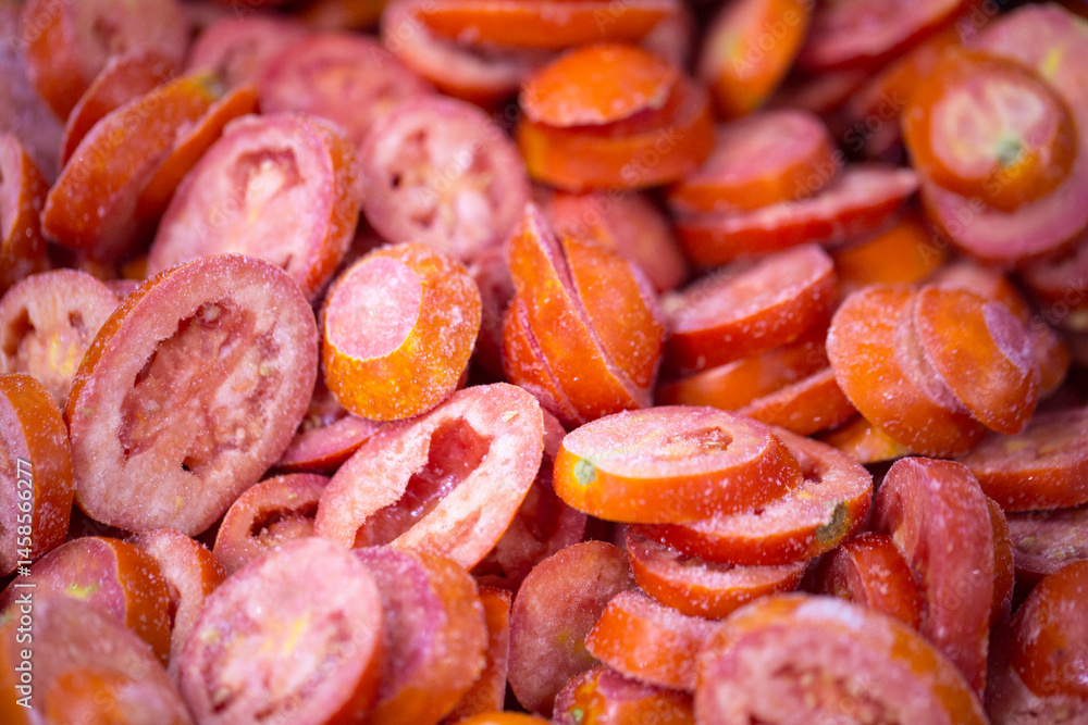 Close-up of shock-frozen sliced red tomatoes with a thin ice coating. Are prepared for retail packaging to ensure extended shelf life in supermarkets and maintain perishable harvest quality.