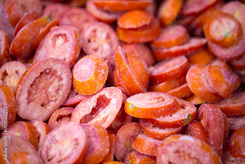 Obraz na płótnie Close-up of shock-frozen sliced red tomatoes with a thin ice coating. Are prepared for retail packaging to ensure extended shelf life in supermarkets and maintain perishable harvest quality. w salonie