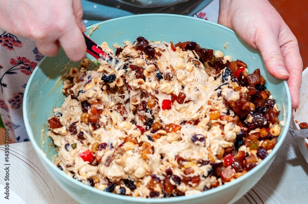 A close-up shot captures hands mixing a bowl of fruitcake batter with a spoon.