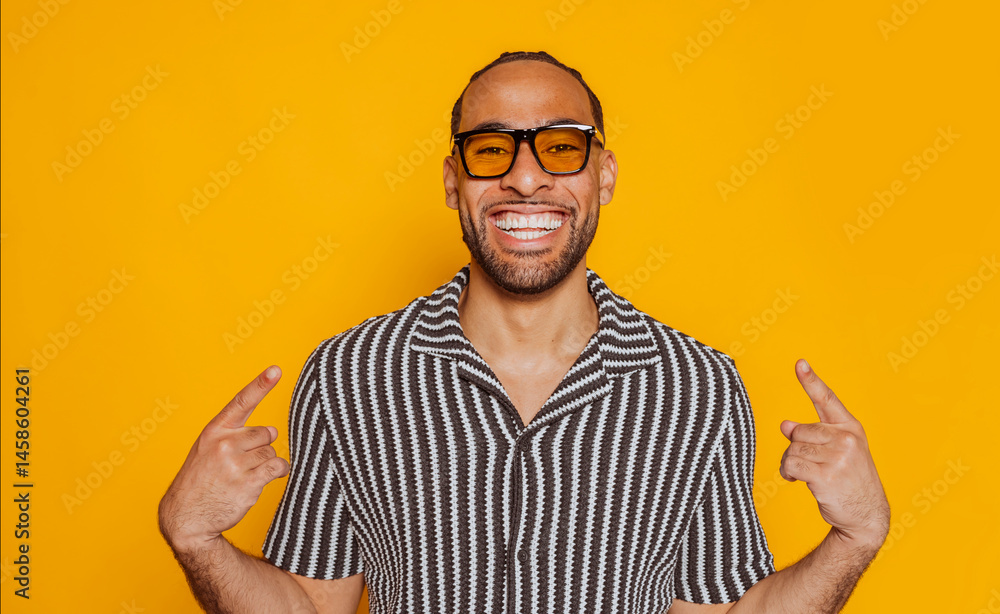 Happy young mixed race man pointing at himself wearing yellow sunglasses and smiling on a yellow background. Happy young mixed race man pointing at himself wearing yellow sunglasses and smiling on a yellow background.