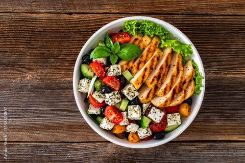 Grilled sliced chicken breast and Greek salad on wooden table	