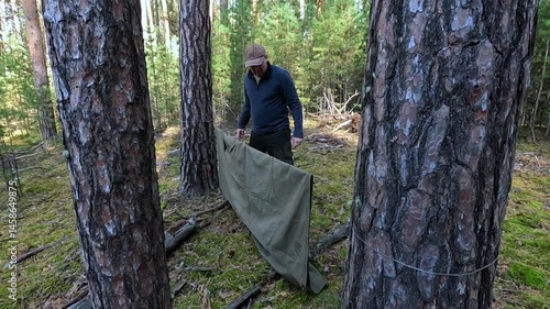 A tourist makes a canopy from an awning in the nature in the forest