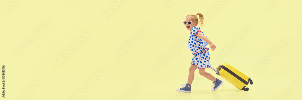 Joyful girl drags yellow suitcase while walking confidently against yellow background, expressing energy and excitement. Concept of childhood, summer trip, joy, activity, motion, adventure.