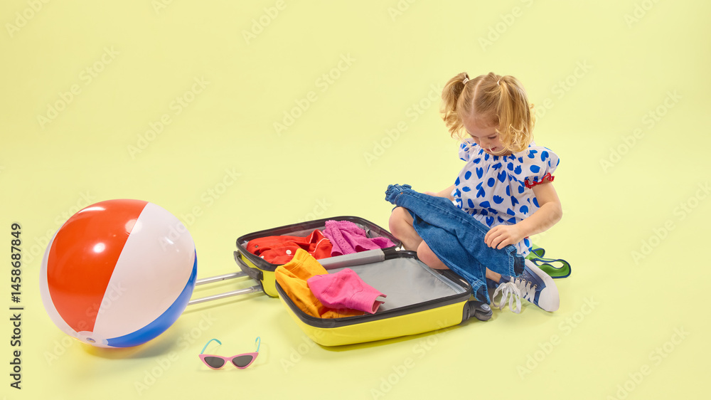 Little girl unpacks colorful clothes from suitcase beside beach ball and sunglasses, showing joy of preparation. Concept of childhood, vacation, color, planning, summer, lifestyle, fun.