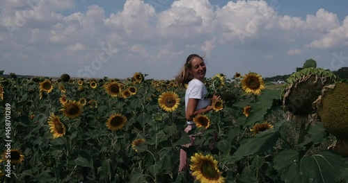A girl in a pink skirt and a white T-shirt walks through a field of blooming yellow sunflowers. A woman dances, rejoices, smiles, enjoys life, warmth, summer, the sun. High quality FullHD footage