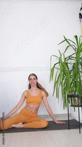 A woman in an orange tracksuit exercises on a yoga mat. On a white background, fitness and muscle building. Stretching, Pilates, and health exercises. High quality FullHD footage