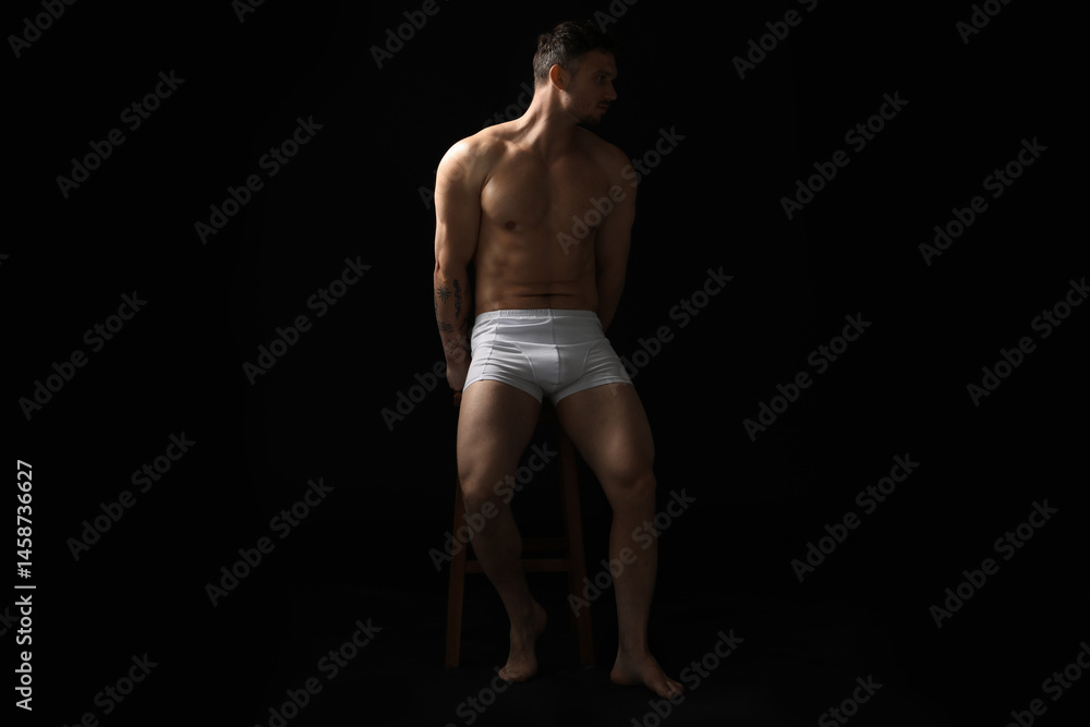 Fototapeta premium Young man in stylish white underwear on chair against black background