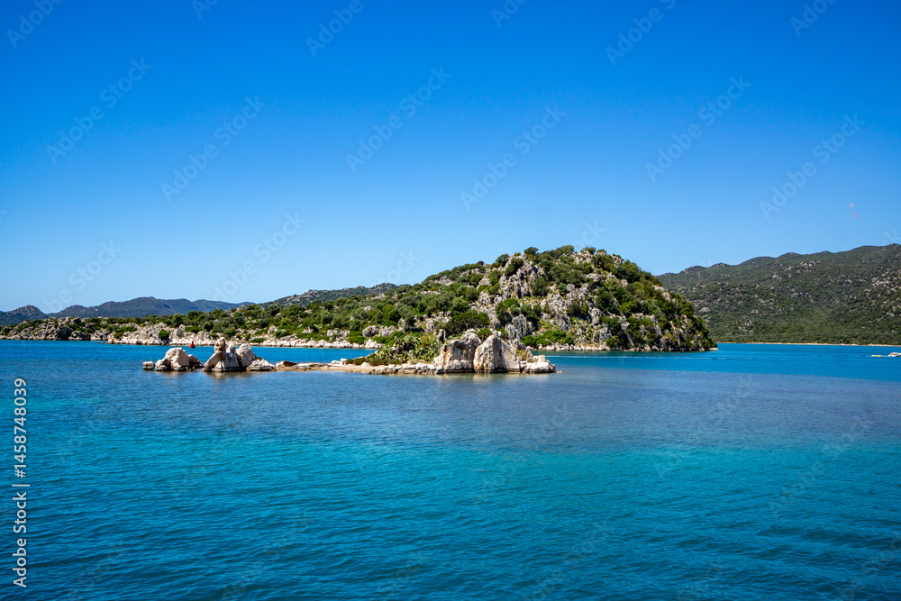 Obraz premium Kekova island reflecting in calm turquoise mediterranean sea under blue sky in Turkey