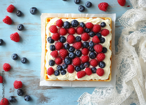 Obraz na płótnie A square waffle with cream cheese and berries, placed on the table, fresh blueberries and raspberries scattered around it. The background is a light sky-blue wooden tabletop,white lace napkins w salonie