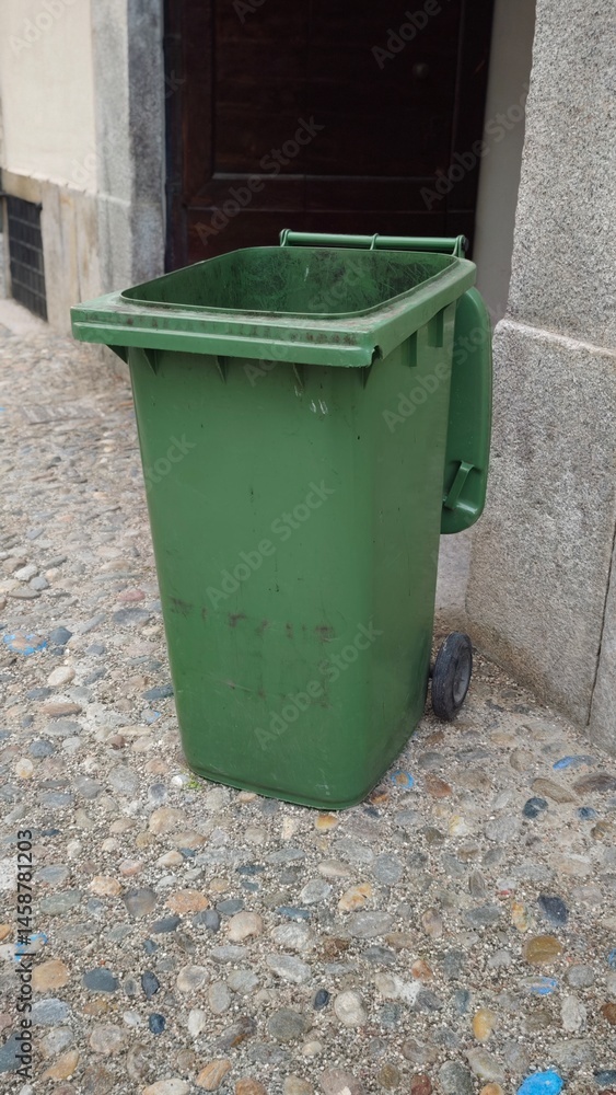 Green Waste Bin on Paved Surface Against Building Entrance Green Waste Bin on Paved Surface Against Building Entrance