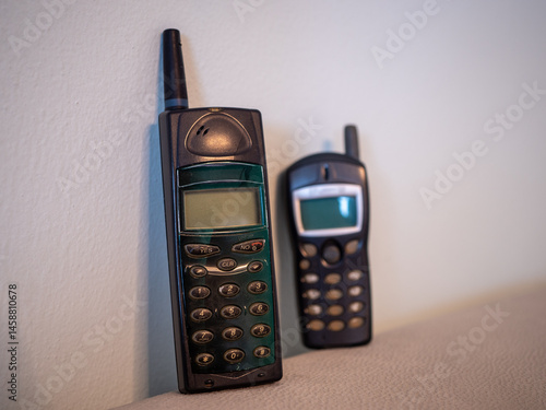 Two old mobile phones, Ericsson A1018s and Alcatel, leaning against a light wall. Classic GSM phones with antennas from the 1990s, shown in a vertical position.