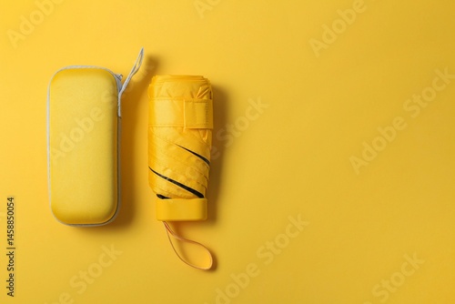 Картината върху платно Bright yellow umbrella  and protective case on yellow background