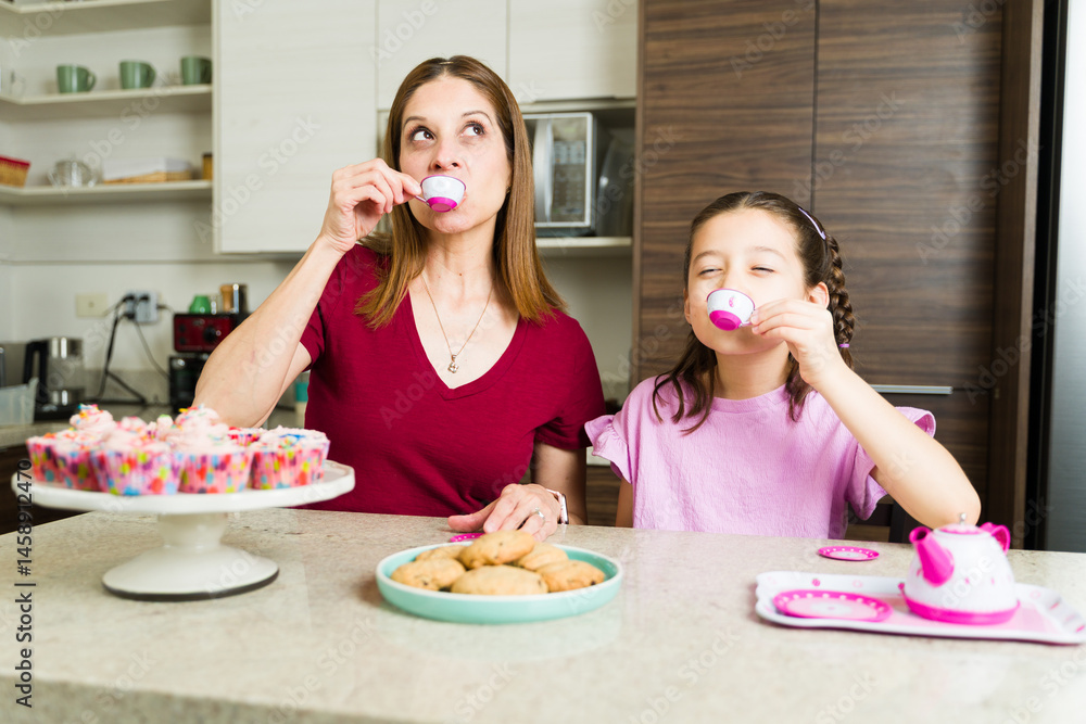 Mother and daughter having fun baking and drinking tea in kitchen