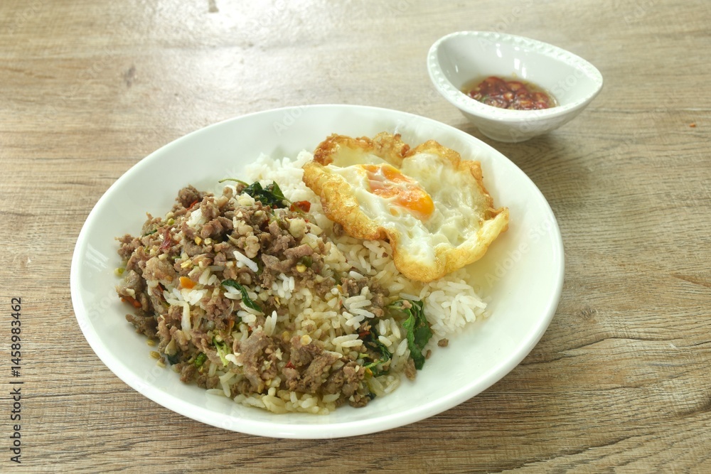 spicy stir fried chop beef meat with basil leaf and chili on rice topping egg in plate dressing fish sauce