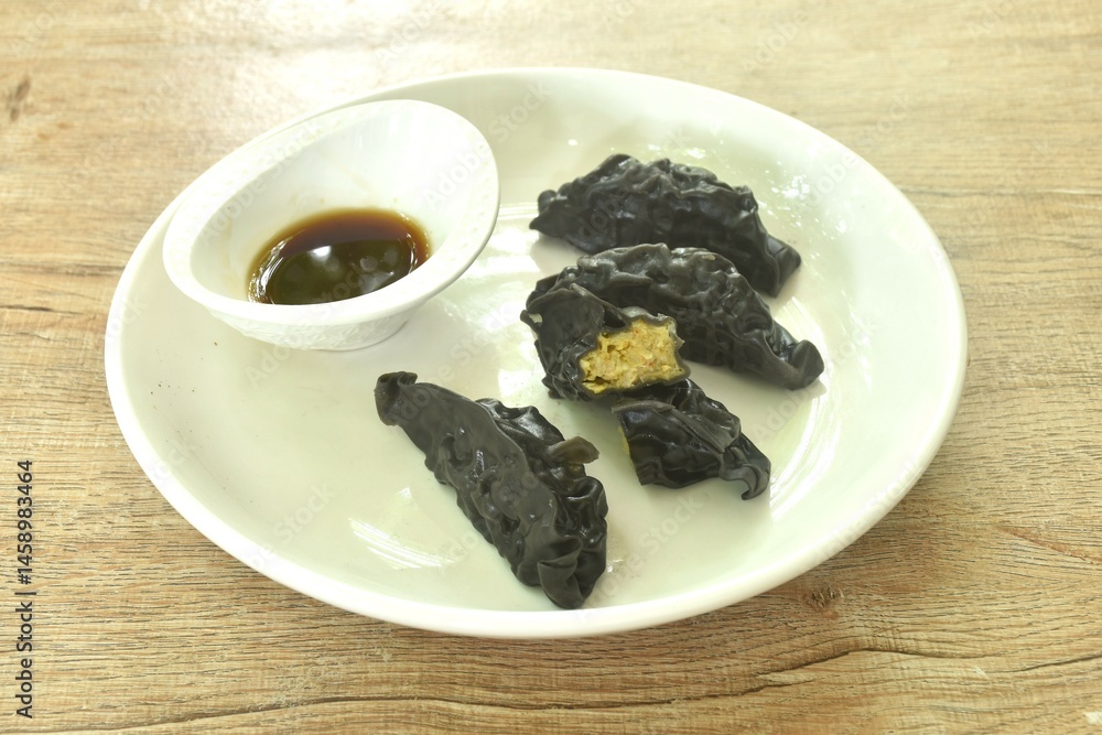 steamed black squid ink Gyoza or Japanese dumpling stuffed mashed pork curry dipping shoyu sauce on plate