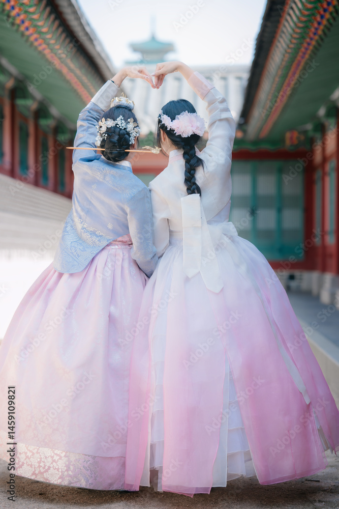 Fototapeta premium Rear view of two young women wearing traditional Korean hanbok making a heart shape with their hands at the historic Gyeongbokgung Palace in Seoul, South Korea.