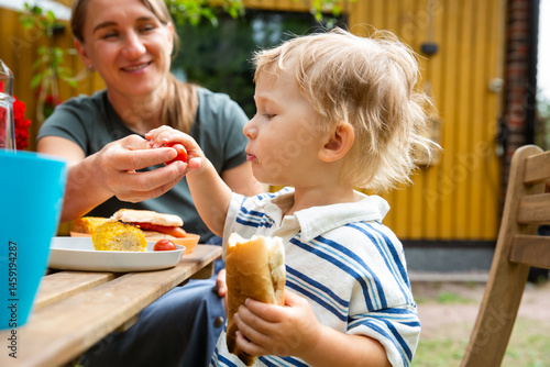 Canvas Print Mother and children eating grilled hot dogs and corn at a backyard table