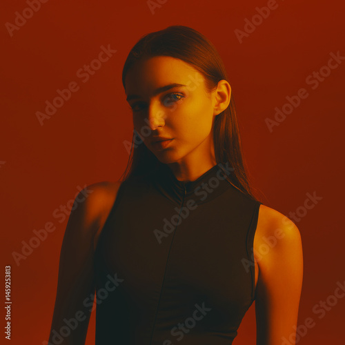 Obraz na płótnie Portrait of beautiful young woman with dark hair, wearing black bodysuit and posing with intense gaze against red background in neon light. Concept of fashion, style, youth culture, trends w salonie