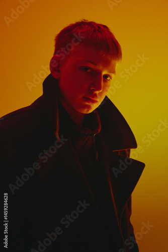Obraz na płótnie Portrait of young man wearing black coat, looking at camera, posing against yellow studio background in neon light. Concept of bold fashion, style, youth culture, self-expression w salonie