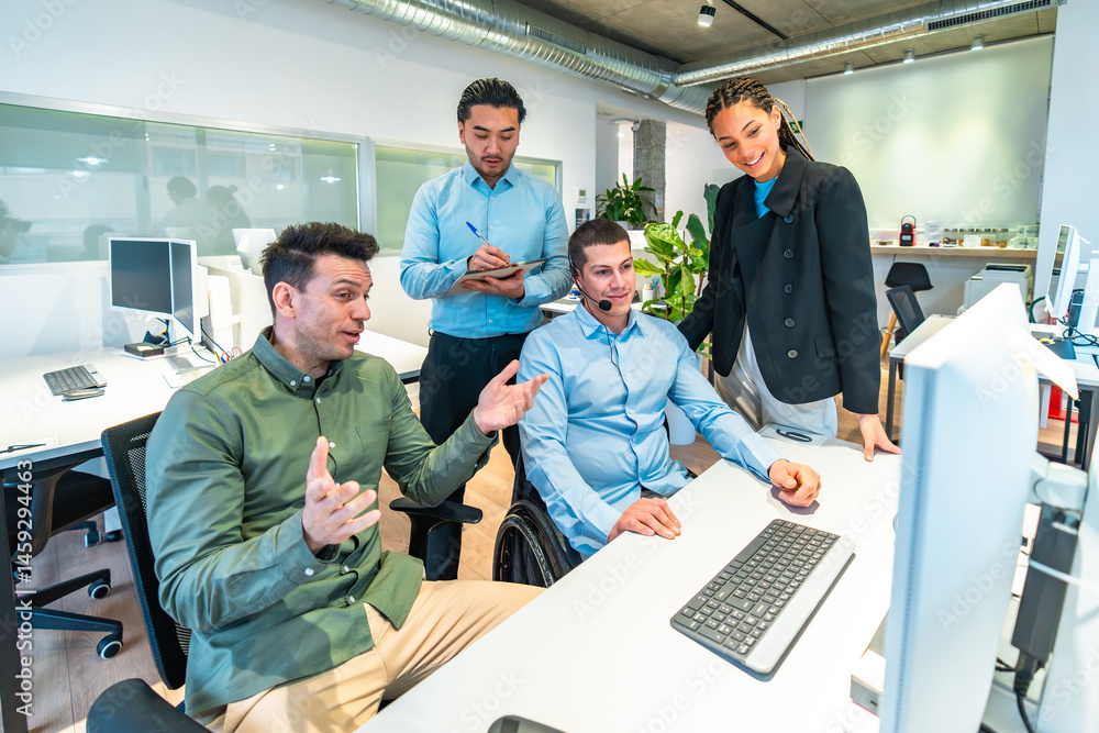 Business team collaborating on computer project with disabled colleague in wheelchair