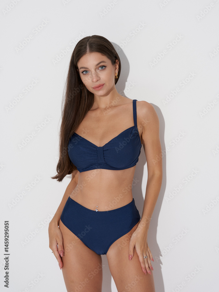 tanned sexy slim woman in blue bikini against white wall tanned sexy slim woman in blue bikini against white wall