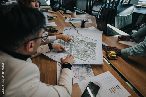 Business professionals engaged in a collaborative discussion about an urban planning project. They are analyzing maps and brainstorming strategies around a conference table in a modern office.
