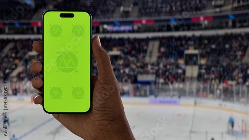 GREEN SCREEN CHROMA KEY A hand holding a phone with a green screen at a hockey game in an indoor stadium, ideal for showcasing live sports or betting apps